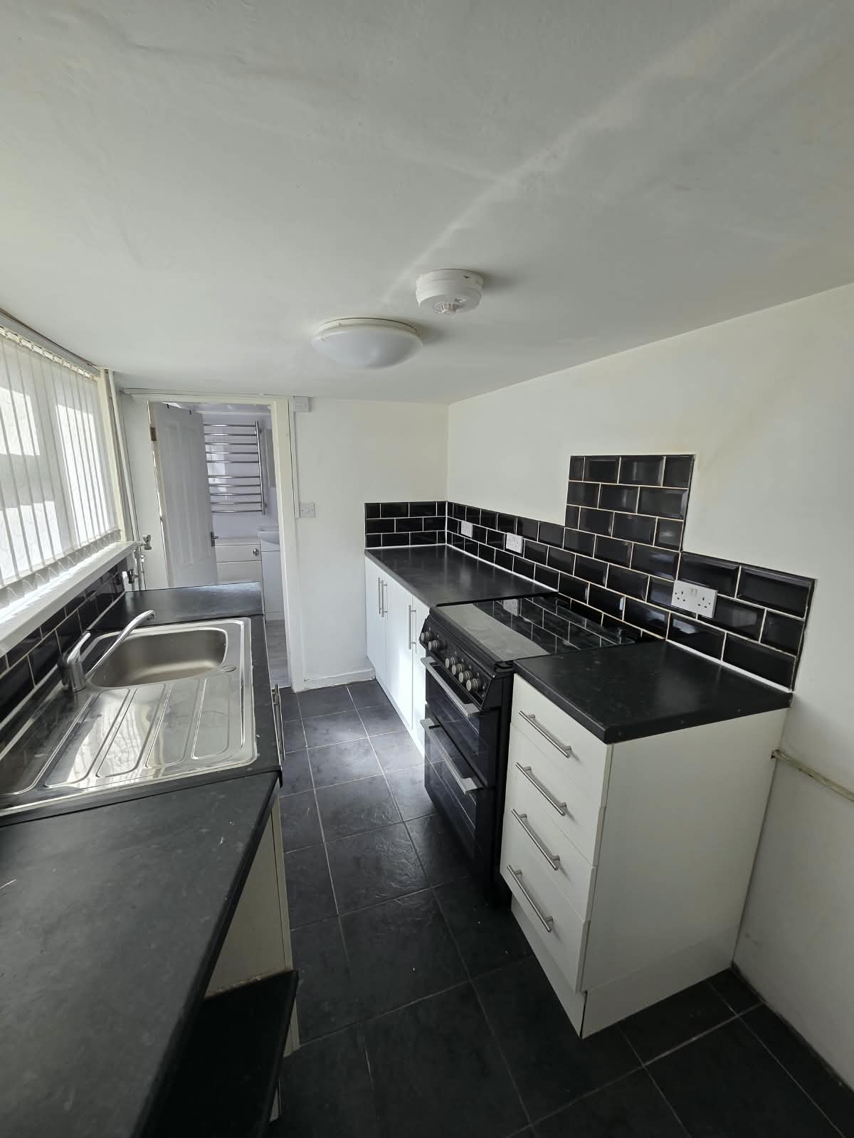 A galley kitchen in a terraced house with a ceiling-mounted heat alarm, photographed on a viewing